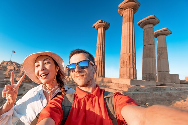 Pareja feliz tomándose una selfie delante de unas columnas griegas antiguas en el Templo de Atenea en Assos, Turquía, bajo un cielo azul soleado