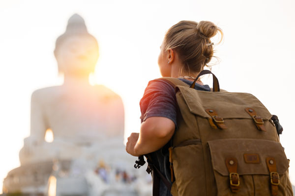 Joven viajera con gran mochila mirando la estatua de un enorme Buda en Phuket, Tailandia, al atardecer.