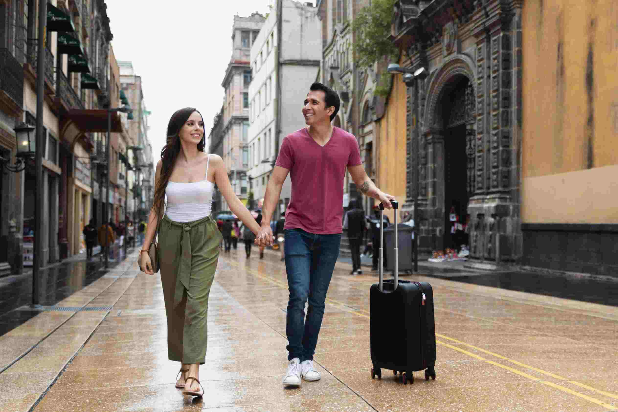 imagem de um homem e uma mulher de mãos dadas, ambos com malas de viagem, em um aeroporto