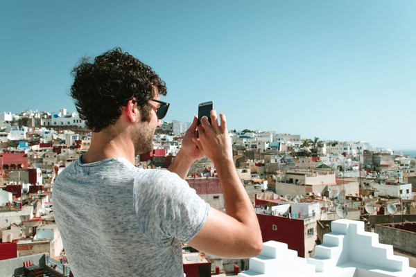 Hombre turista tomando fotografías con smartphone de la ciudad vieja de Tánger desde una altura en un día soleado