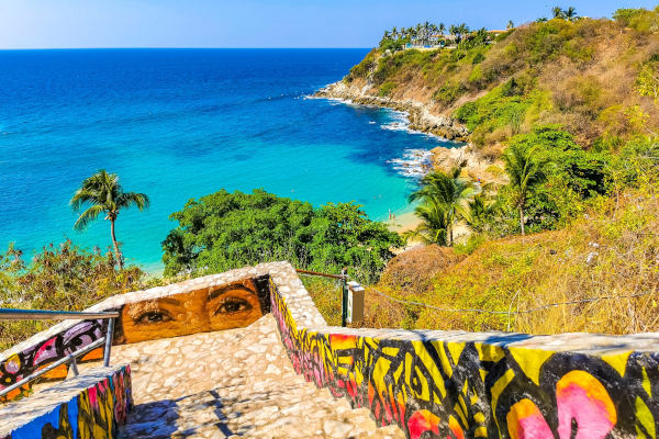 Escalinata de piedra con pinturas rumbo a la Playa Carrizalillo con vegetación de fondo.