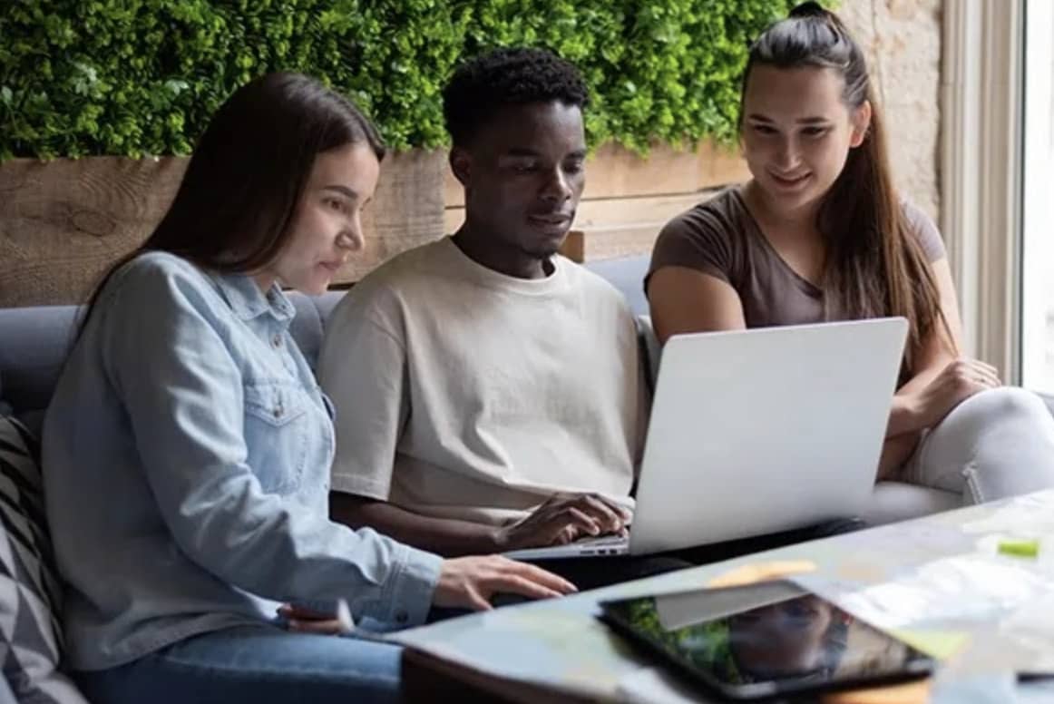 duas mulheres e um homem utilizando notebook para contratar seguro viagem