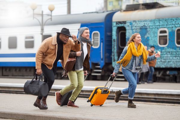 imagem de uma mulher e dois homens, com malas de viagem, correndo em uma estação de trem durante viagem de trem pela Europa