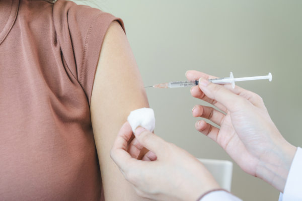 Profesional de la salud aplicando vacuna en el antebrazo de una persona con fondo claro liso.