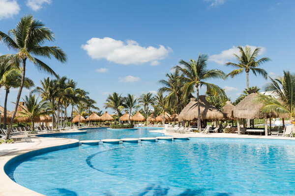  imagem de um resort em Cancún, no México, com piscina em primeiro plano, bangalôs e árvores ao fundo
