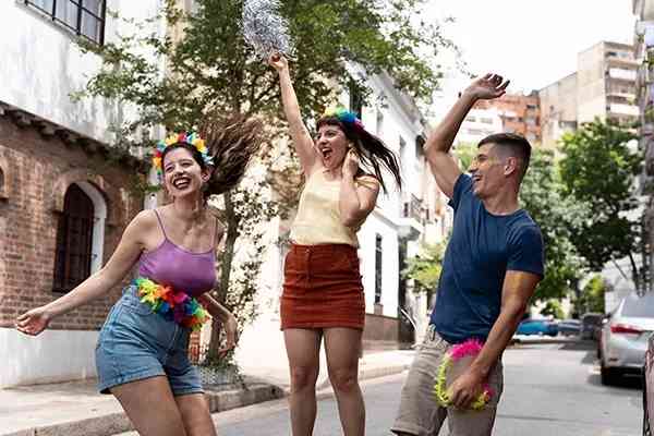 Duas mulheres e um homem pulam e brincam fantasiados em Carnaval de rua