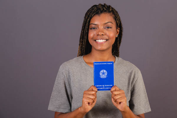 Mulher jovem brasileira segurando carteira de trabalho e previdência social. Documento oficial.