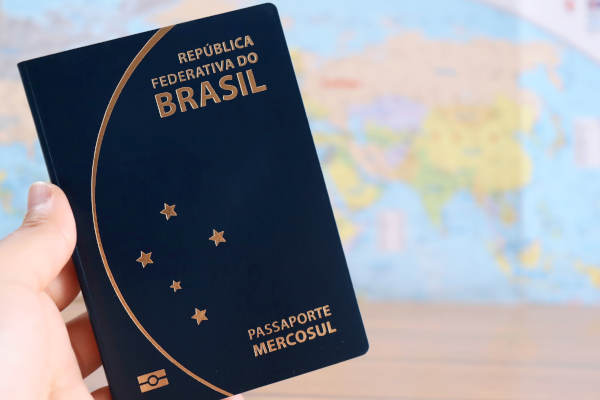Mulher segurando passaporte brasileiro com mapa-múndi ao fundo.