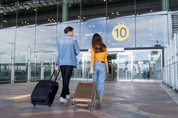 Vista trasera de la pareja joven caminando en la terminal del aeropuerto a la puerta de embarque con una maleta cada uno.