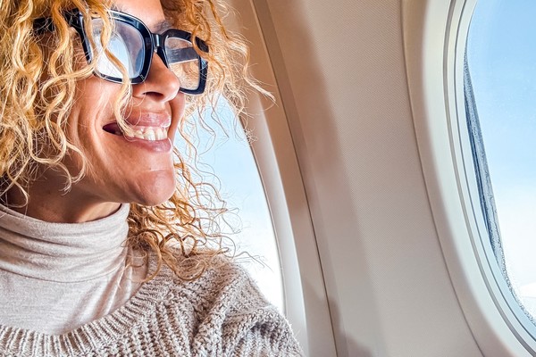 Mujer feliz viajando en avión junto a la ventanilla.