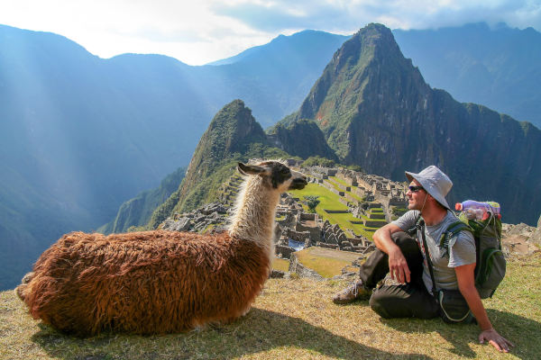 Turista en Machu Picchu con una llama en primer plano y las ruinas incas al fondo.