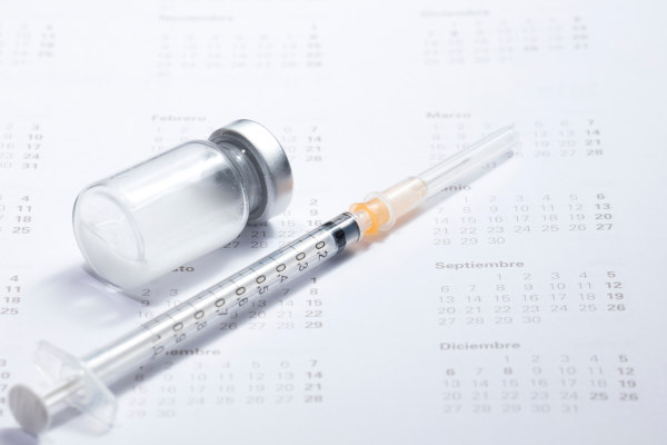 Vial de vacuna vacío y jeringa sobre un calendario físico en referencia al calendario de vacunación.