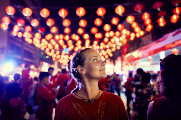 Mujer turista sonriente disfrutando de un mercado nocturno en China, con luces brillantes y coloridas de fondo.