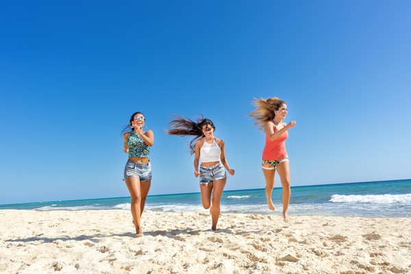 Tres mujeres felices corriendo por la playa en un día soleado.