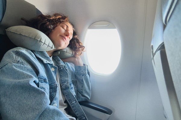 Mujer durmiendo tranquila con cuello de viaje en el asiento de un avión.