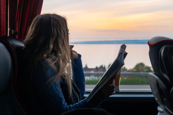 Chica joven leyendo un libro mientras mira por la ventana del bus el atardecer.