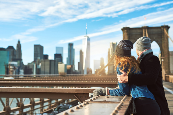 Pareja abrigada en invierno mirando el skyline de Nueva York desde el puente de Brooklyn en un día soleado, Nueva York, Estados Unidos.