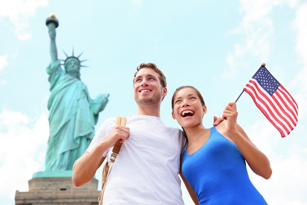 Pareja posando feliz con bandera de Estados Unidos con la Estatua de la Libertad de fondo.