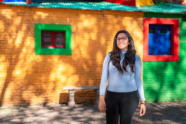 Mujer latina sonriendo frente a las coloridas casas de Caminito, ubicadas en el barrio La Boca de Buenos Aires.