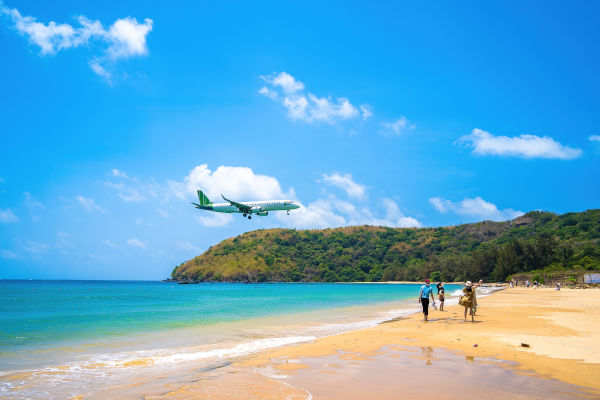 Turistas caminando por la playa Dam Trau con un avión pasando por encima.