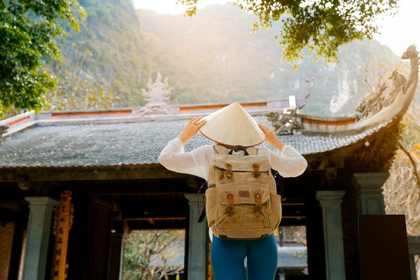 Mujer turista con sombrero cónico asiático explorando un antiguo templo en Ninh Binh, Vietnam.