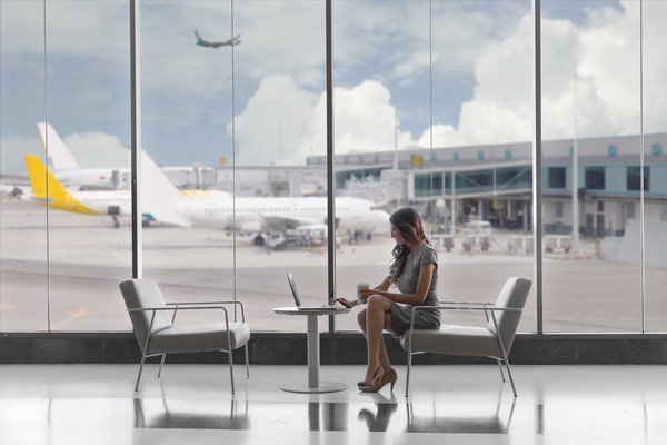 Mujer de negocios trabajando con laptop en una mesa sentada en un sillón cómodo de una sala VIP transparente de un aeropuerto con aviones de fondo.