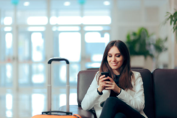 Mujer sonriente viendo su celular en el aeropuerto