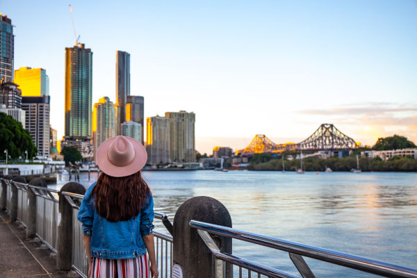Mujer con sombrero contemplando el atardecer sobre los rascacielos de Brisbane desde Kangaroo Point, junto al río Brisbane, en Queensland, Australia.