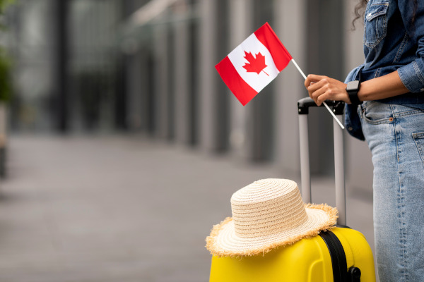 Persona sosteniendo una maleta y una bandera de Canadá en un aeropuerto, lista para viajar.