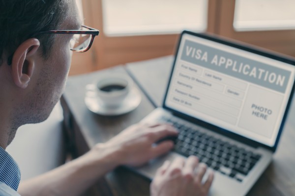 Hombre utilizando una laptop para hacer una solicitud de visa de forma electrónica en un sitio web genérico.