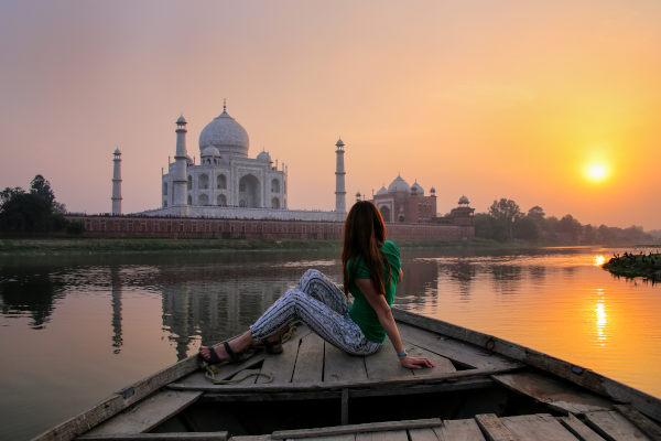 Mujer turista en el borde de un bote viendo la puesta del sol sobre el Taj Mahal, Agra, India.