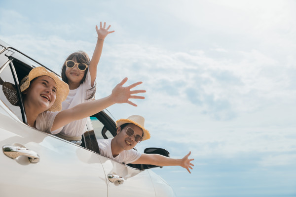 Familia sonriente disfrutando de un viaje en auto al aire libre en un día soleado.