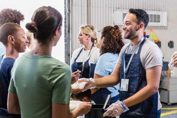 Voluntarios alegres y diversos sirven comida en un comedor.