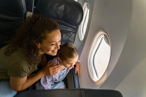 Mãe e filha dentro de avião sorrindo enquanto olham pela janela.
