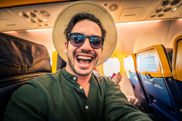 Turista masculino sonriente tomándose una selfie en el interior de un avión.