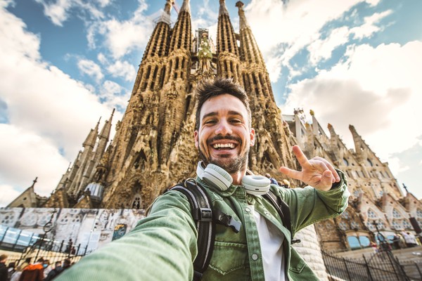 Turista masculino tomándose una selfie con la fachada de La Sagrada Familia de fondo en Barcelona, España.