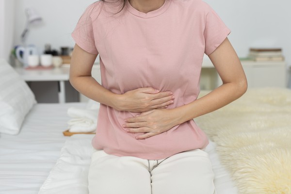Mujer sosteniéndose la barriga adolorida sentada en una cama, con diarrea tras visitar una de las playas contaminadas en Brasil.