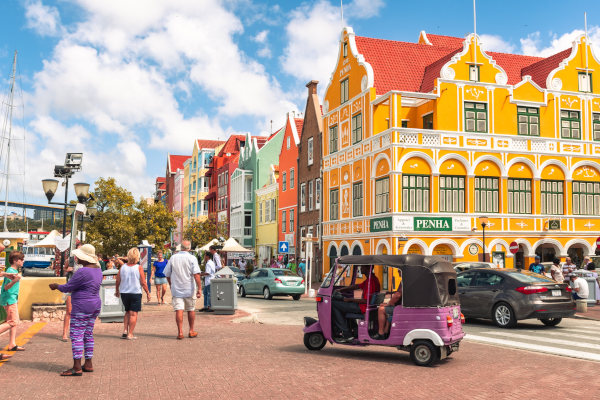 Calles de Willemstad con gente, coches y típicos edificios coloridos de Curazao en un día soleado.