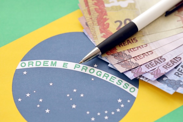 Reales brasileños en efectivo con una lapicera junto a la bandera de Brasil.