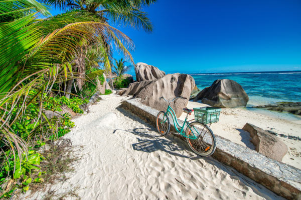 Una bicicleta, medio de transporte principal en varias islas de Seychelles, detenida en una playa de arena blanca con rocas y vegetación alrededor.