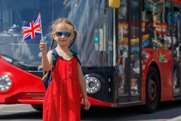 Niña turista con gafas de sol y el cabello trenzado alzando una bandera en miniatura del Reino Unido en un día soleado en Londres, Inglaterra.