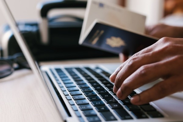 Persona con pasaporte en mano, que ingresa al portal de la Unión Europea para tramitar el ETIAS