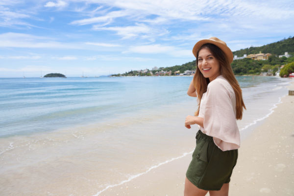 Mujer joven en la playa de Florianópolis, Brasil, mirando a cámara y sonriendo.