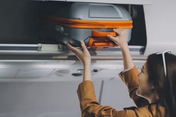 Mujer que coloca su equipaje de mano en el compartimento superior del avión.
