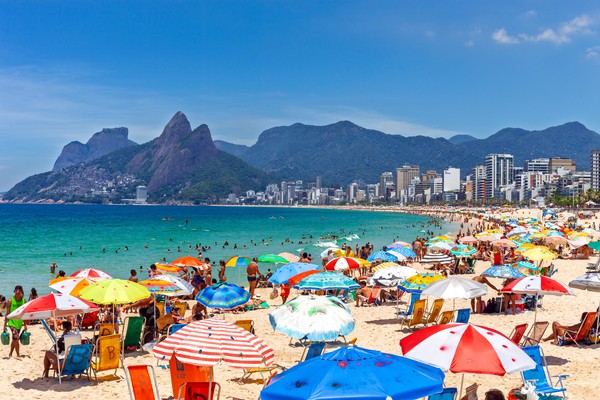 Vista de la playa de Ipanema en Río de Janeiro, Brasil, con múltiples sombrillas de colores y gente bañándose en el mar en un día soleado.