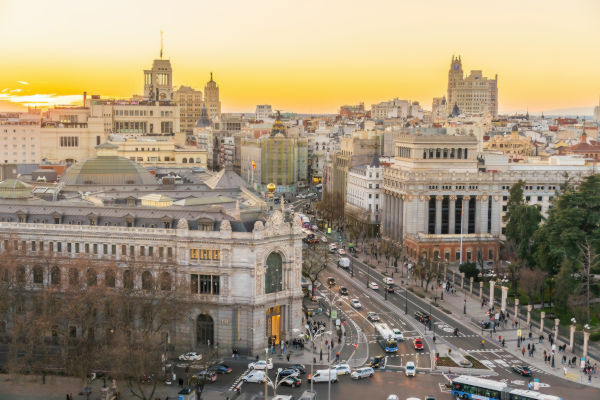 Vista panorámica del centro de Madrid al atardecer, con edificios históricos, tráfico en movimiento y calles iluminadas.