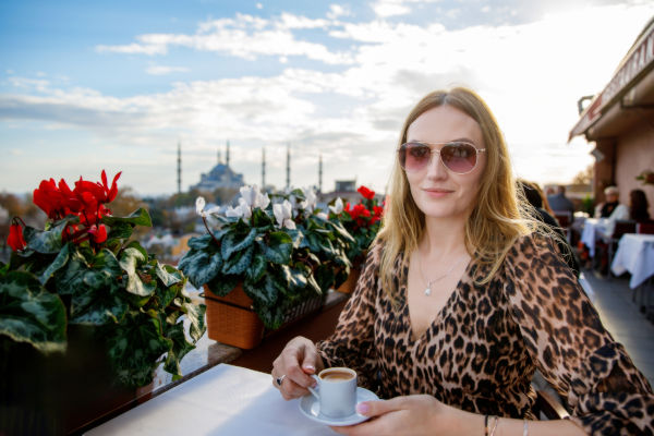 Turista disfrutando un café en una terraza con vista a la Mezquita Azul de Estambul al atardecer.