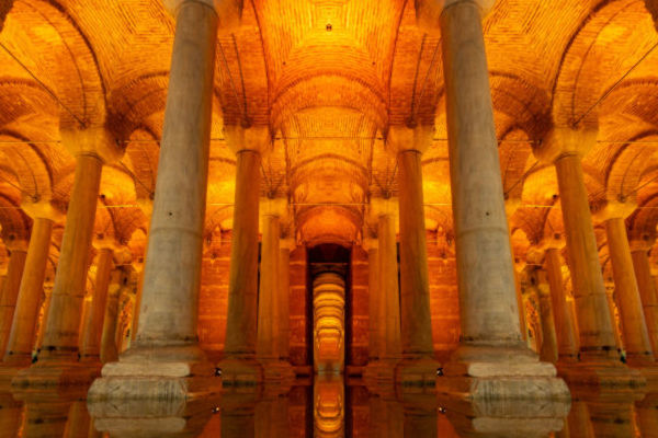 Interior iluminado de la Cisterna Basílica en Estambul, con columnas reflejadas en el agua y techos abovedados de ladrillo.