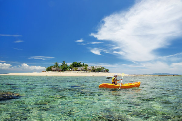 Joven haciendo kayak en una canoa amarilla en aguas poco profundas cerca de Isla del Mar del Sur, grupo de islas Mamanuca, Fiji.