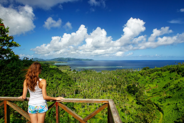 Mujer turista de espaldas en un mirador del Parque de la Herencia Nacional de Bouma en la isla Taveuni, Fiji, observando la vegetación en un día soleado.